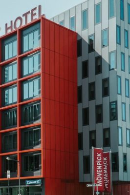 Contemporary architectural design of a hotel with striking red and grey facade in a city setting.
