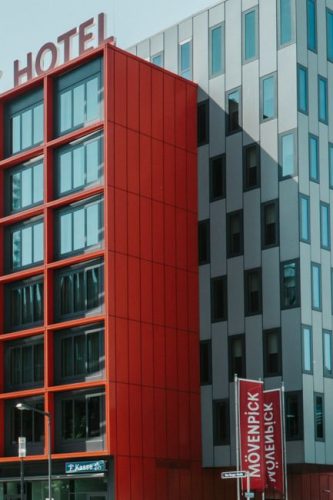 Contemporary architectural design of a hotel with striking red and grey facade in a city setting.